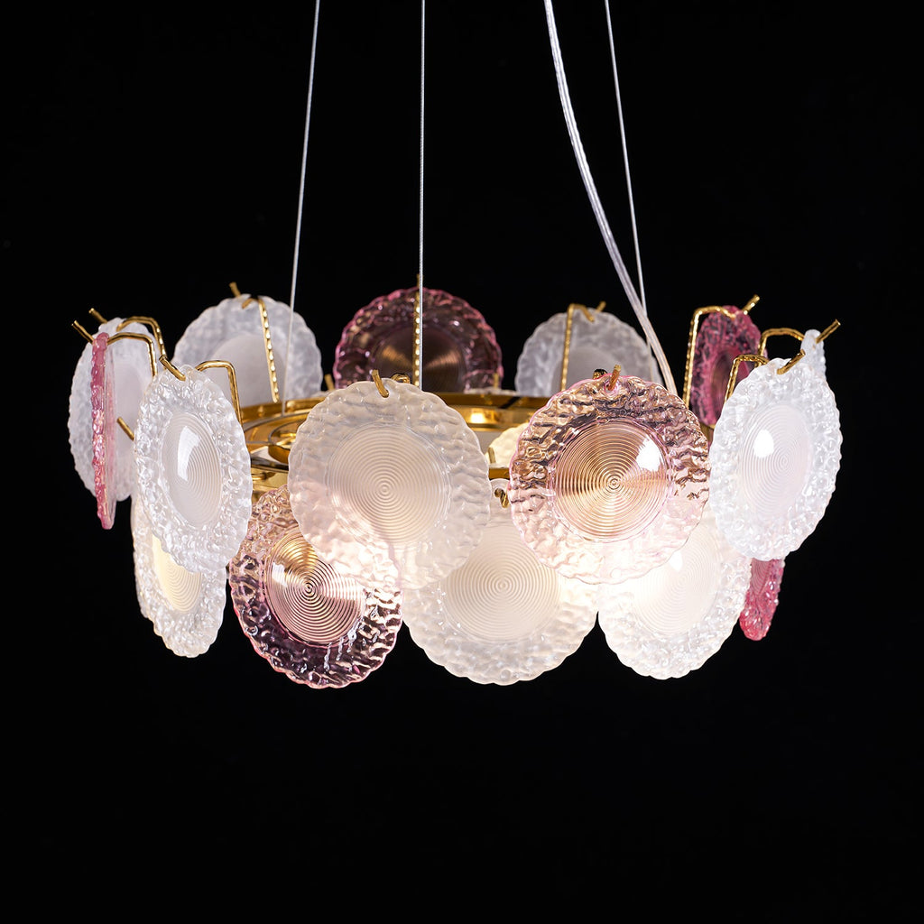 This Clérachic pendant lit on a black backdrop, with pink and frosted glass discs on a gold ring and two white wires above.