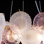 Close view of frosted and pink glass discs on gold hooks, with a darker background, on this Clérachic pendant.