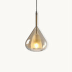 Amber glass teardrop pendant from Clérachic on a plain white backdrop, with a frosted inner shade lit warm and a slim brass stem above.