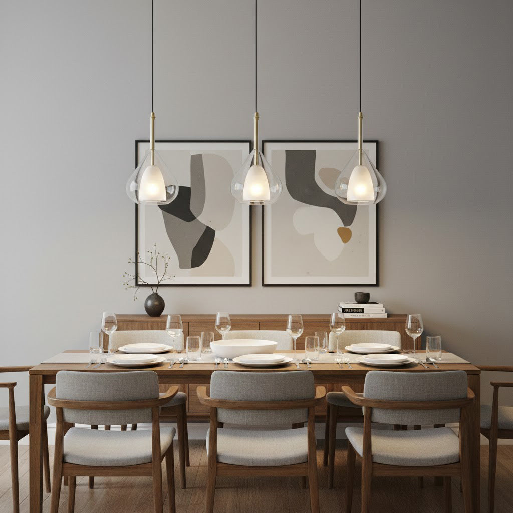 Three Clérachic glass pendants hung in a row above a walnut dining table with grey upholstered chairs, in front of two abstract prints.