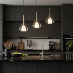 Three Clérachic clear glass pendants lit above a black marble kitchen island, with dark cabinets and a white tiled splashback behind.
