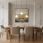 Three Clérachic glass pendants lit at staggered heights above a pale oak dining table, in front of a gold and charcoal abstract painting.