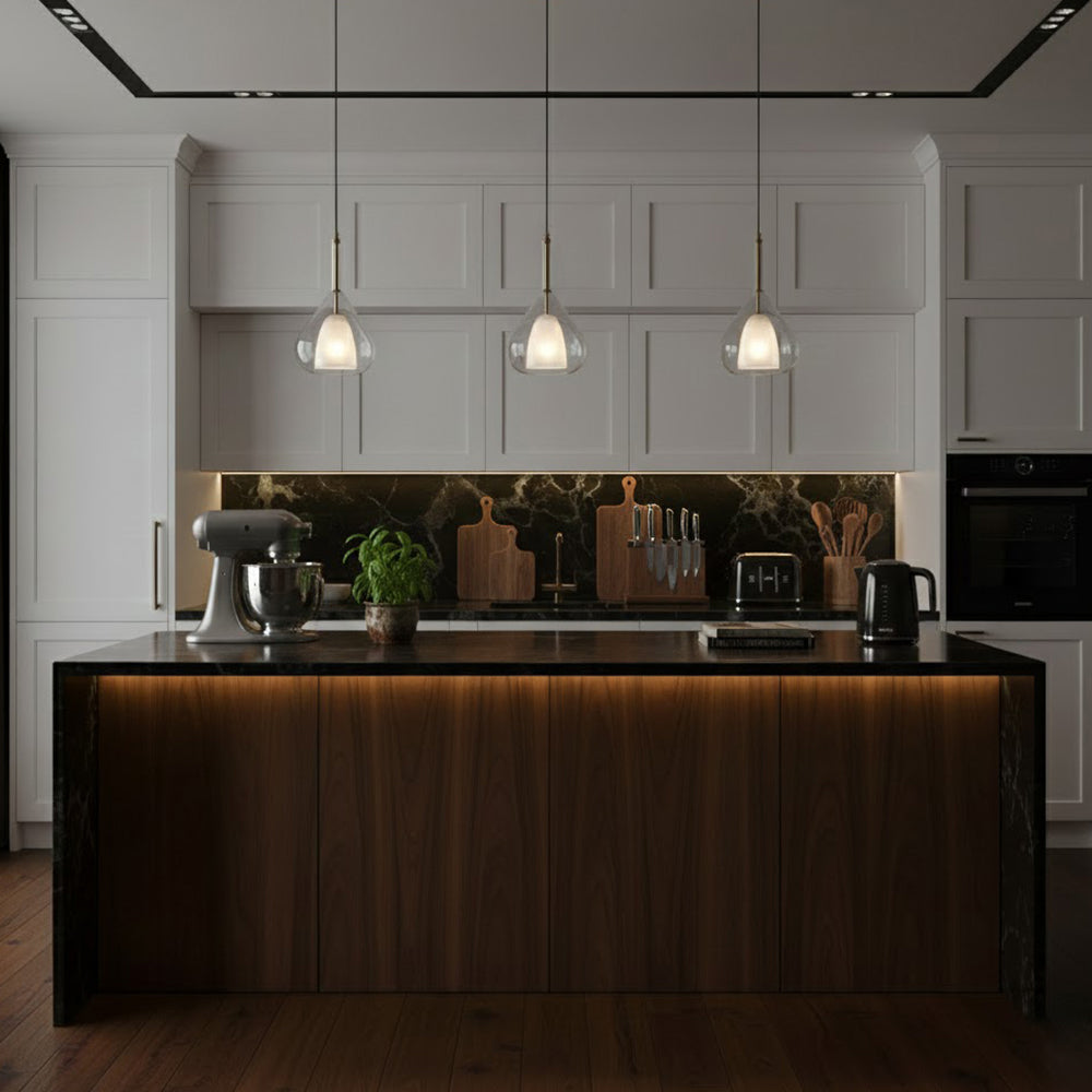 Three Clérachic glass pendants hung over a dark wood kitchen island with an under-counter glow, with white shaker cabinets behind.