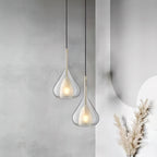 Two Clérachic clear glass pendants at different heights against a soft grey wall, with dried pampas grass in the corner.