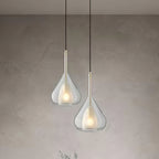 Two Clérachic clear glass pendants at different heights against a limewashed grey wall, each with a frosted inner shade and a warm glow.