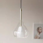 Close view of a clear glass teardrop pendant from Clérachic, with a frosted inner shade, a brass stem and black cord, against a pale wall.