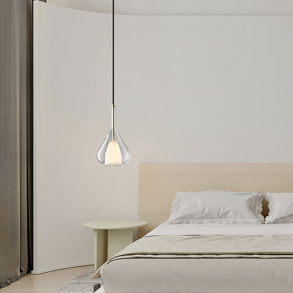 Clérachic clear glass pendant lit over a pale bedroom with a low bed, a round green side table and a curved wall.