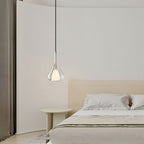 Clérachic clear glass pendant lit over a pale bedroom with a low bed, a round green side table and a curved wall.