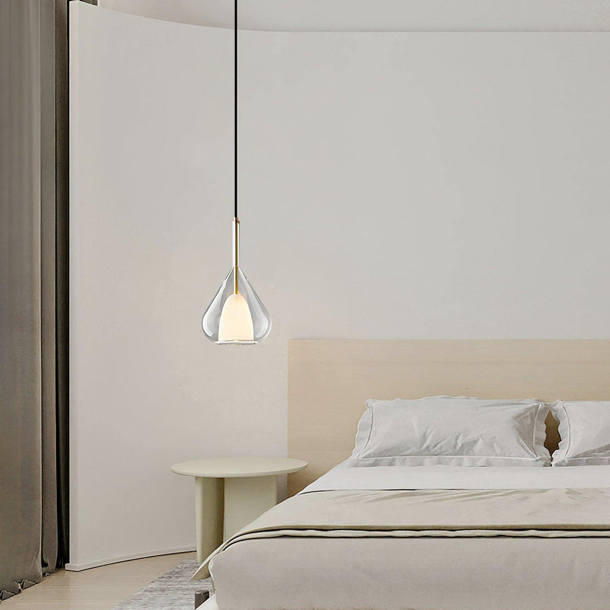 Clérachic clear glass pendant lit over a pale bedroom with a low bed, a round green side table and a curved wall.