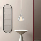 Clérachic clear glass pendant lit beside a tall black-framed oval mirror, with a pale conical table below, seen from a slightly wider angle.