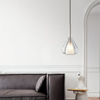 Clérachic clear glass pendant lit in a white room with an arched opening, above a dark leather sofa with a cushion.