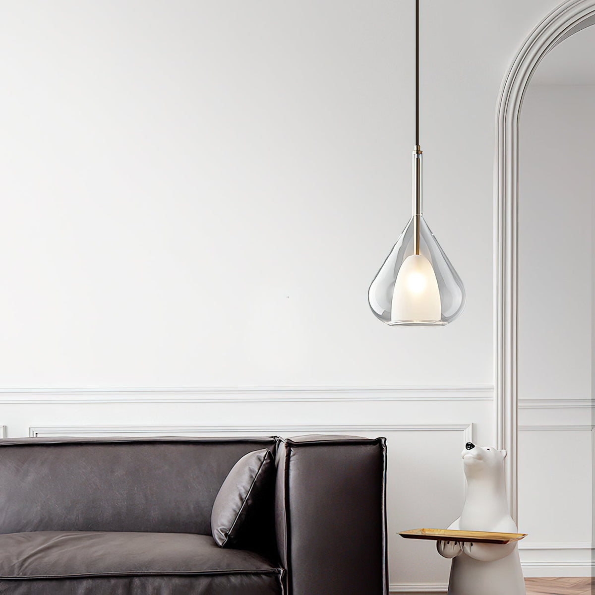 Clérachic clear glass pendant lit in a white room with an arched opening, above a dark leather sofa with a cushion.