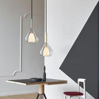 Two Clérachic clear glass pendants at different heights in a room with grey wall mouldings and a dark angular panel, above a small table.
