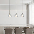 Three Clérachic clear glass pendants in a row above a marble-topped counter with taupe chairs, beside sheer curtains.
