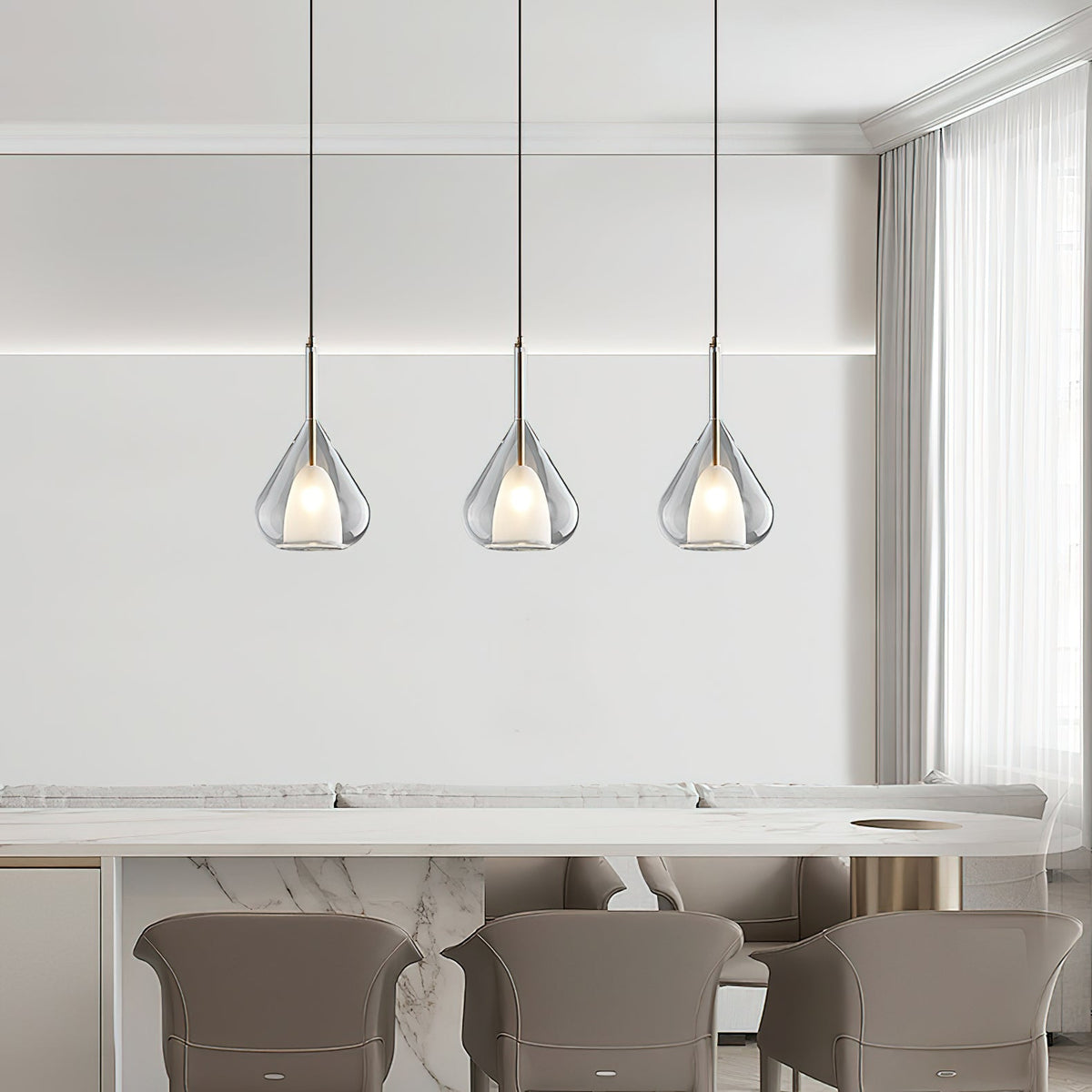 Three Clérachic clear glass pendants in a row above a marble-topped counter with taupe chairs, beside sheer curtains.