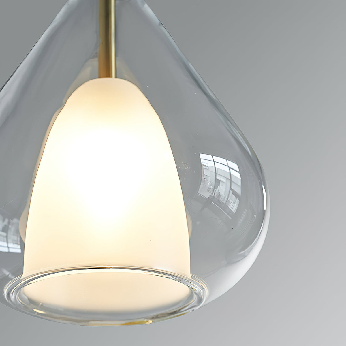 Close view of the frosted white inner shade and clear outer glass of this Clérachic pendant, with a brass stem above.