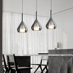 Three Clérachic smoke grey glass pendants lit above a dark stone dining counter, in front of sheer white curtains.