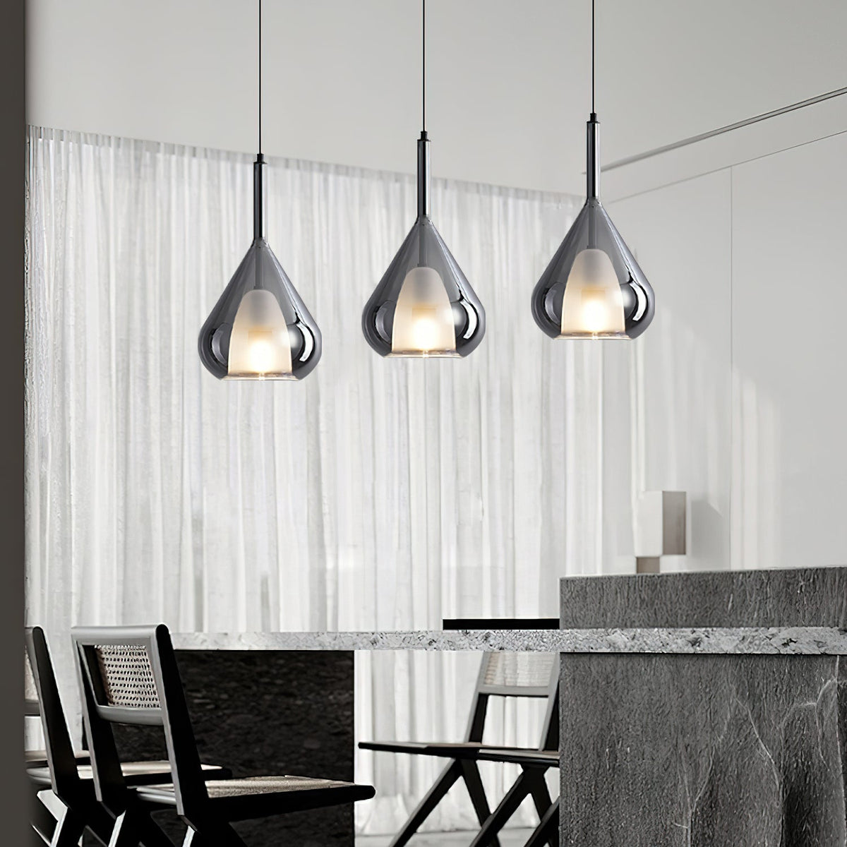 Three Clérachic smoke grey glass pendants lit above a dark stone dining counter, in front of sheer white curtains.