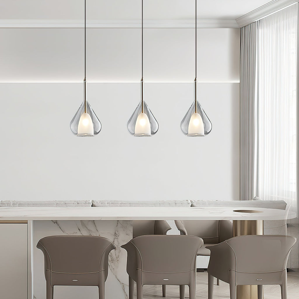 Three Clérachic clear glass pendants in a row above a marble-topped counter with taupe chairs, seen from further back.