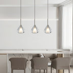 Three Clérachic clear glass pendants in a row above a marble-topped counter with taupe chairs, seen from further back.