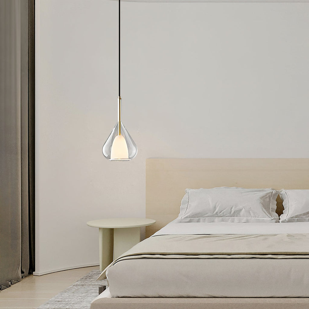 Single Clérachic clear glass pendant above a low bed with cream bedding, a pale round side table and heavy curtains at the left.