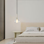 Single Clérachic clear glass pendant above a low bed with cream bedding, a pale round side table and heavy curtains at the left.