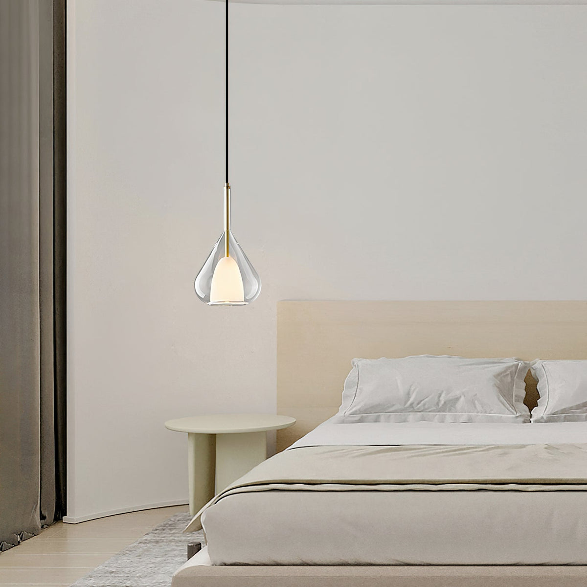 Single Clérachic clear glass pendant above a low bed with cream bedding, a pale round side table and heavy curtains at the left.