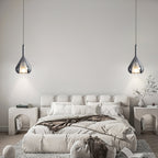 Two Clérachic smoke grey glass pendants lit either side of a tufted cream bed, with arched bedside tables and a dried branch.