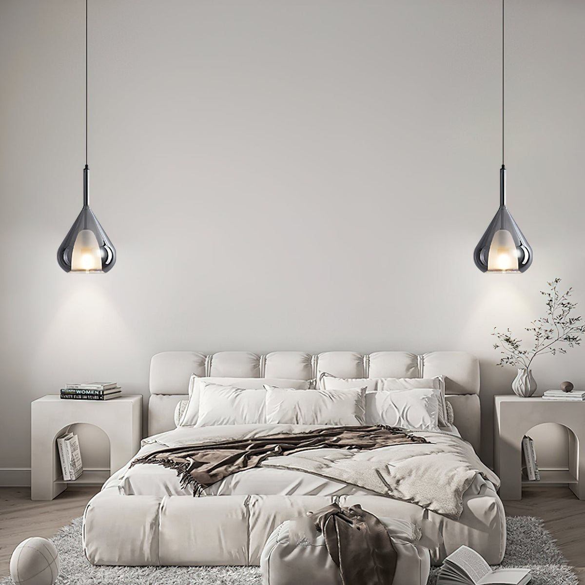 Two Clérachic smoke grey glass pendants lit either side of a tufted cream bed, with arched bedside tables and a dried branch.