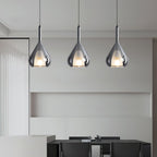 Three Clérachic smoke grey glass pendants above a black dining table, with a built-in shelf niche in a grey wall behind.