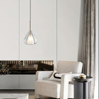 Clérachic clear glass pendant lit beside a cream armchair and a dark round side table, in a room with a fireplace and long curtains.