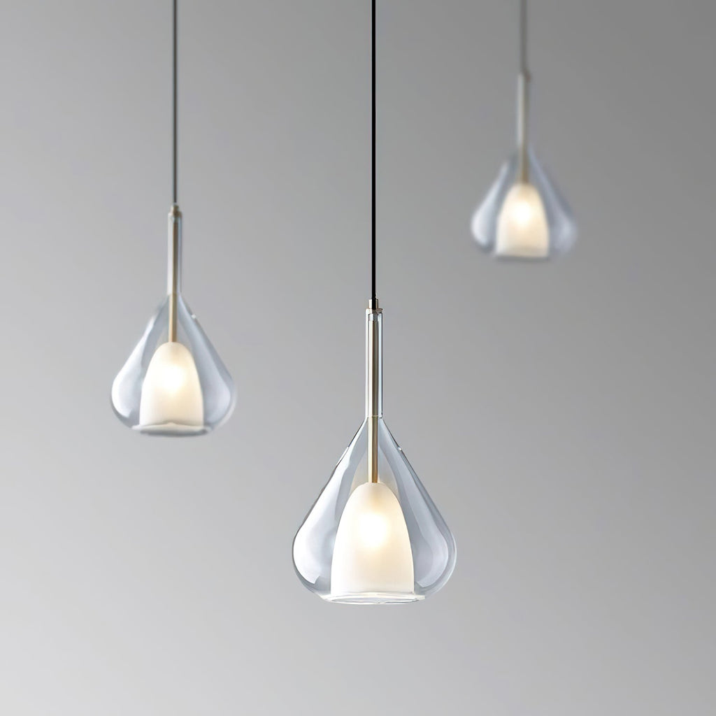 Three Clérachic clear glass pendants at staggered heights against a graduated grey backdrop, each lit with a warm frosted inner shade.