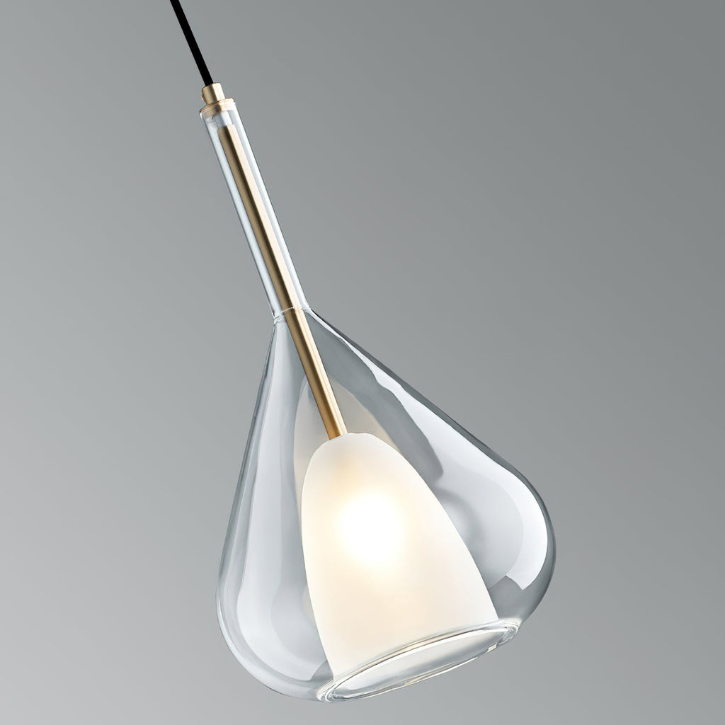 Clérachic clear glass pendant seen at an angle against a grey backdrop, showing the brass stem and the lit frosted shade inside.