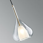 Clérachic clear glass pendant seen at an angle against a grey backdrop, showing the brass stem and the lit frosted shade inside.