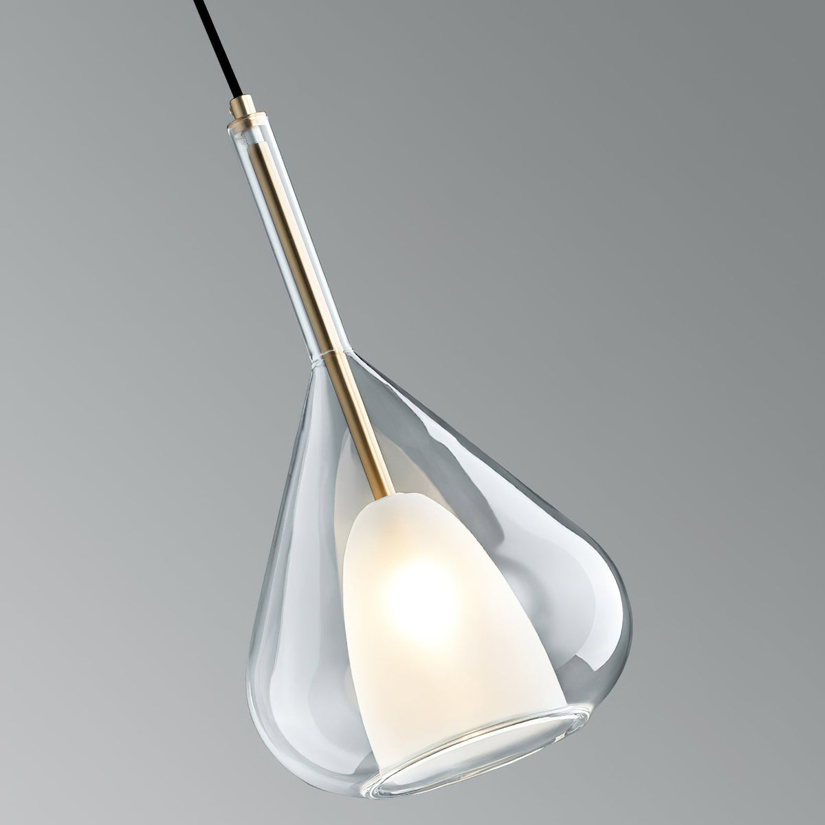 Clérachic clear glass pendant seen at an angle against a grey backdrop, showing the brass stem and the lit frosted shade inside.