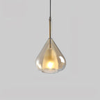 Amber glass teardrop pendant from Clérachic on a pale grey backdrop, with a lit frosted inner shade and a dark metal stem above.