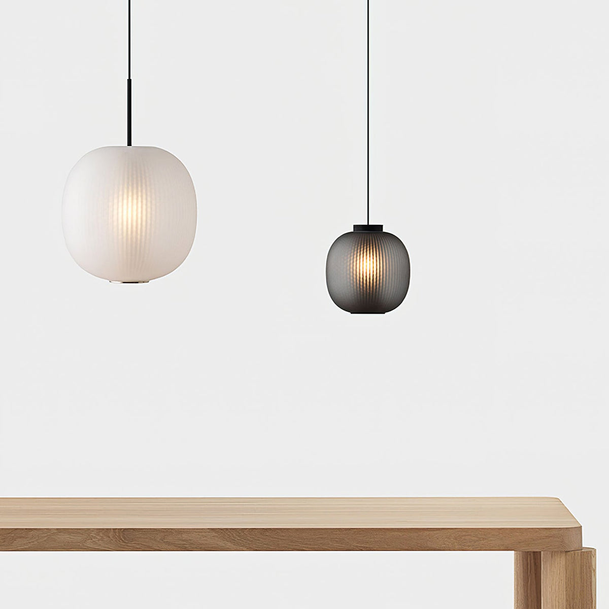 Two Clérachic ribbed glass pendants of different sizes, one matte white and one smoke grey, hanging above a pale oak bench.