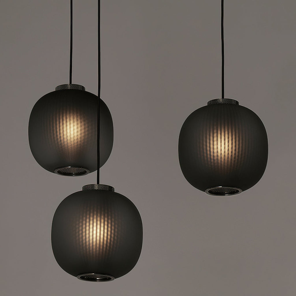 Three smoke-grey Clérachic ribbed glass pendants hung at different heights, each lit from within, against a muted grey wall.