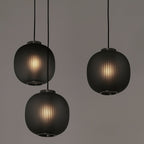 Three smoke-grey Clérachic ribbed glass pendants hung at different heights, each lit from within, against a muted grey wall.