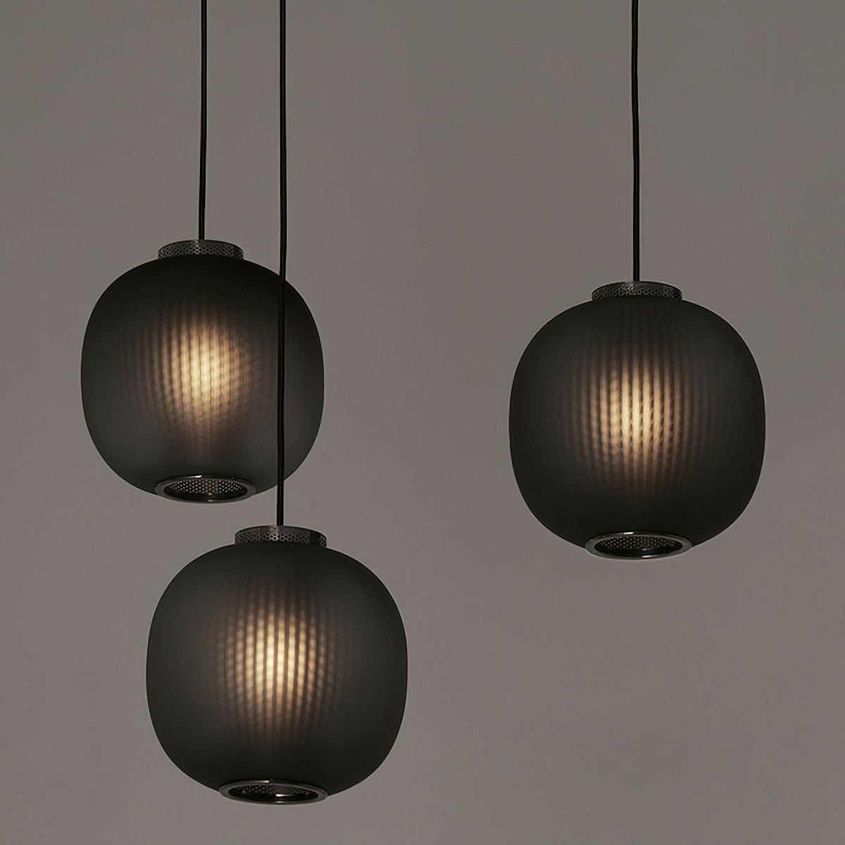 Three smoke-grey Clérachic ribbed glass pendants hung at different heights, each lit from within, against a muted grey wall.