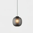 Single smoke-grey Clérachic pendant glowing softly against a pale backdrop, its ribbed glass hanging from a thin black cord.