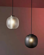Matte white and smoke-grey Clérachic glass pendants hanging together against a terracotta-red wall, both lit.