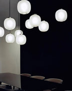Cluster of matte white Clérachic glass pendants glowing against a dark wall, above a long dark table with chairs.
