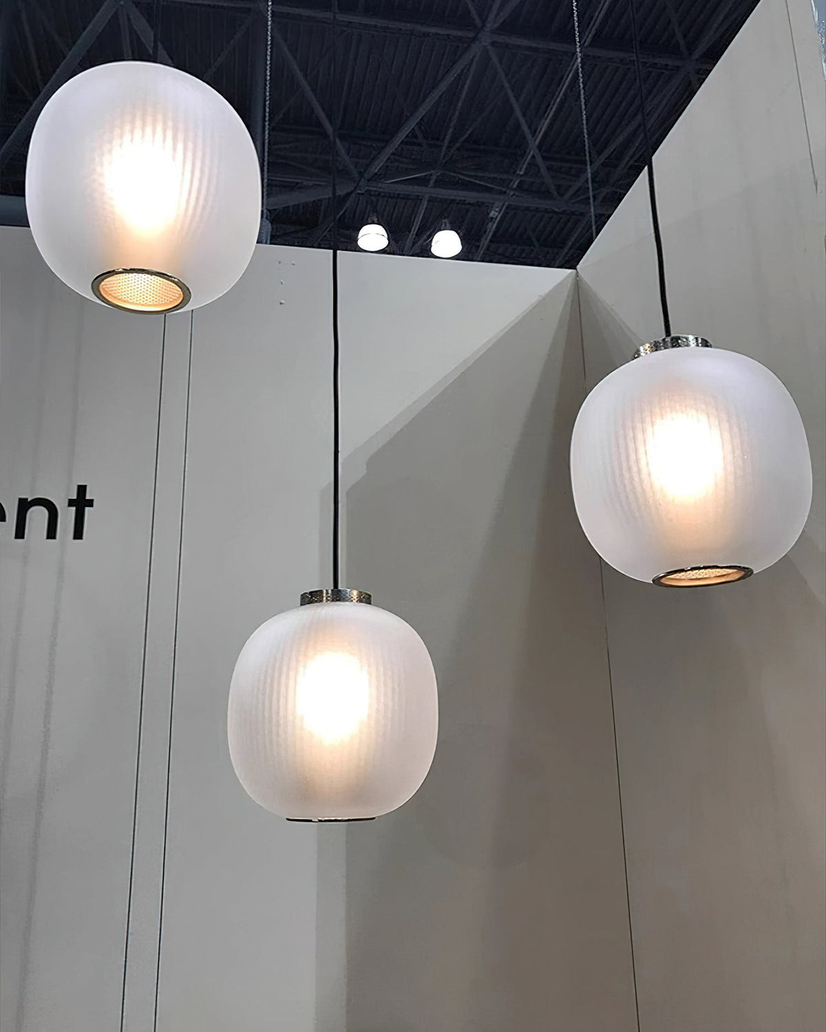 Three lit matte white Clérachic pendants at different heights in a high-ceilinged showroom with a pale grey wall.