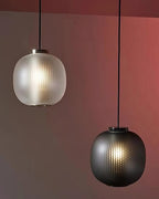 A matte white and a smoke-grey Clérachic pendant hung at different heights against a rust-coloured wall.
