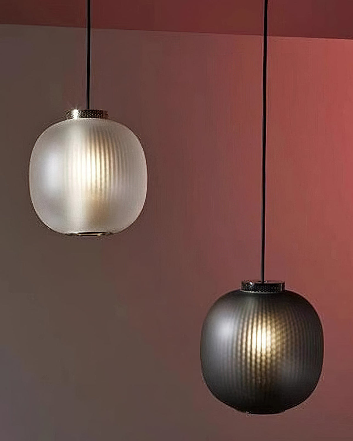 A matte white and a smoke-grey Clérachic pendant hung at different heights against a rust-coloured wall.