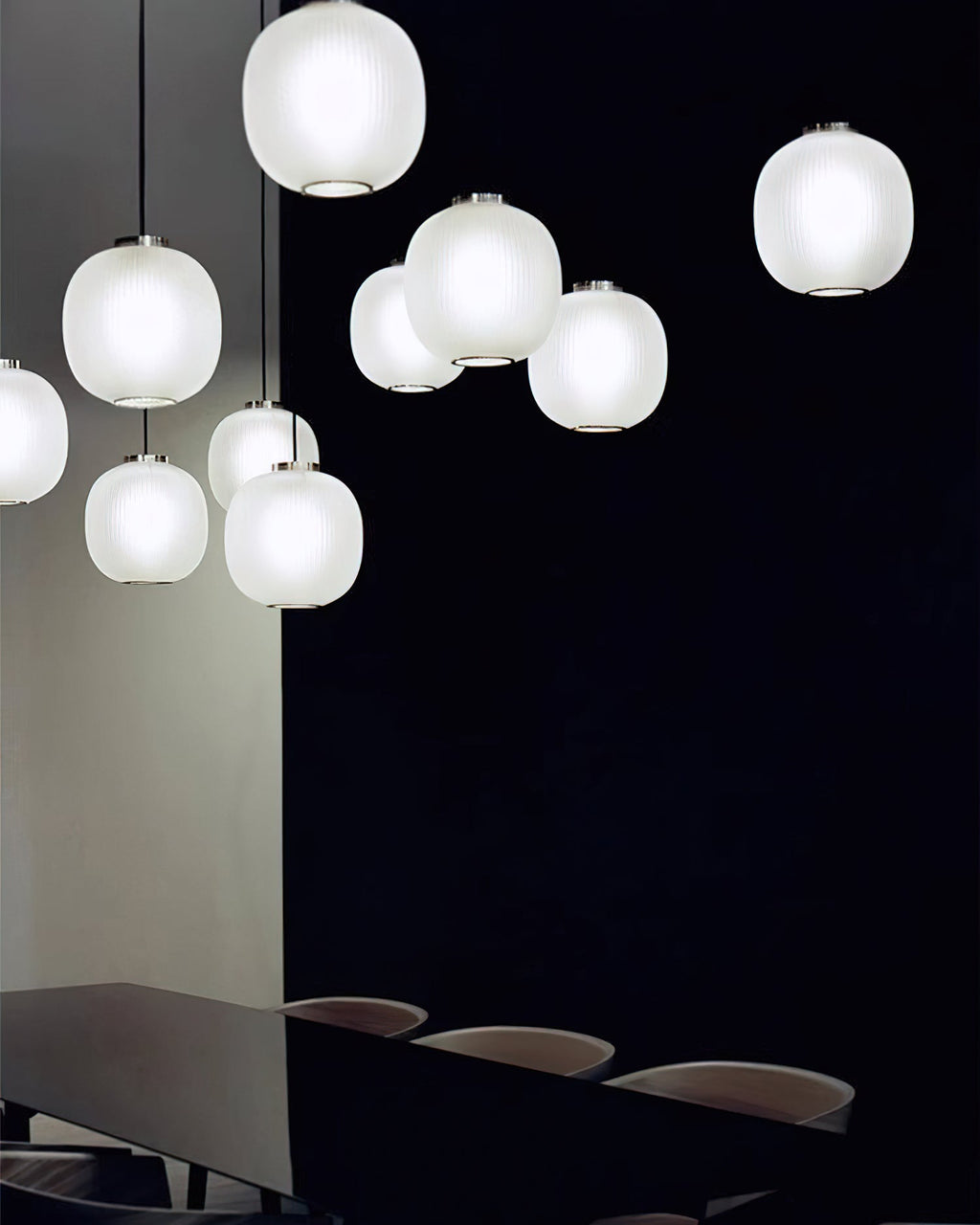 Matte white Clérachic ribbed glass pendants in a loose cluster against a dark wall, with a dark table below.