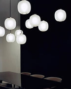 Matte white Clérachic ribbed glass pendants in a loose cluster against a dark wall, with a dark table below.