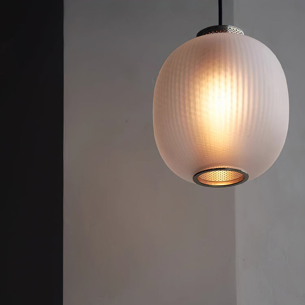 Close view of a lit matte white ribbed glass shade on this Clérachic pendant, warm light glowing inside and a metal mesh ring below.