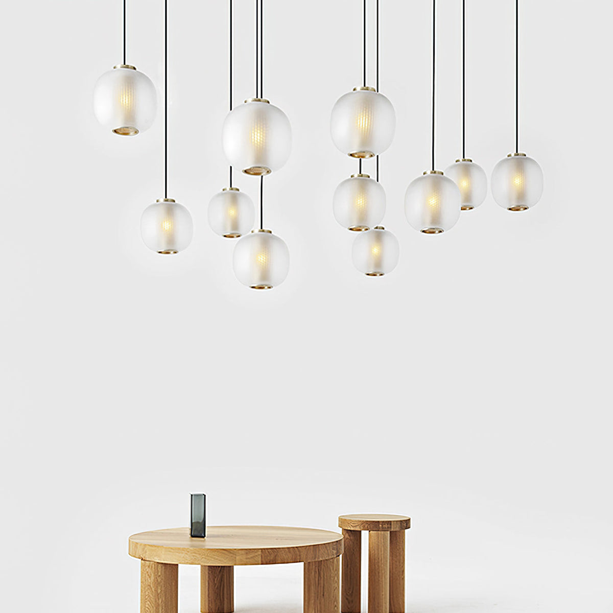 Cluster of small matte white Clérachic pendants at varied heights above two round oak side tables on a white wall.